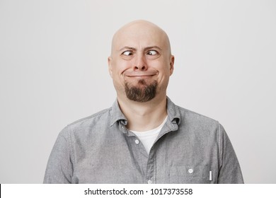 Portrait Of Funny And Childish Bald Caucasian Male Model Making Crazy Eyes And Smiling Strangely, Standing Over Gray Background. Guy Shows Daughter That He Can See His Own Nose Without Mirror