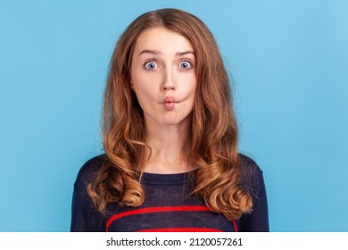 Portrait of funny crazy woman standing and looking with crossed eyes and fish lips, having fun, humor, wearing striped casual style sweater. Indoor studio shot isolated on blue background.