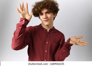 Portrait Of Funny Cute Teenger With Curly Hair Posing Isolated Gesturing With Both Hands. Handsome Young Man In Casual Shirt Making Awkward Gesture, Dancing, Showing Something, Waving At Camera