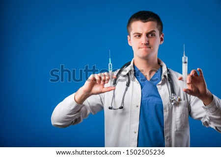 Portrait of funny emotional male doctor with two syringes isolated on blue background