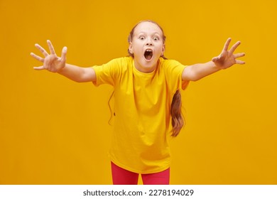 Portrait of a funny fair-haired girl child in colourful summer clothes looking with big surprise at the camera. Studio shot on a yellow background. Children and emotions.