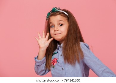 Portrait Of Funny Female Kid Having Long Auburn Hair Looking On Camera Giving High Five, Meaning Hi Or Bye With Hand Over Pink Background