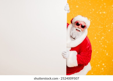 Portrait of funny funky christmas father in red hat headwear look behind white wall poster advertise winter x-mas shopping seasonal miracle sales discounts isolated over bright color background - Powered by Shutterstock