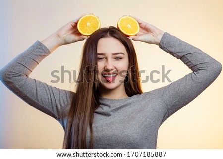 portrait of funny girl with orange halves like ears over head, woman fooling around, showing tongue teasing, concept fruits and vitamins,positive mood