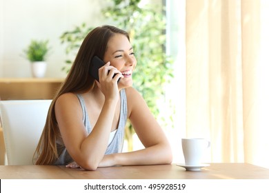 Portrait Of A Funny Girl Taking A Phone Conversation Sitting In A Table At Home And Looking Through The Window