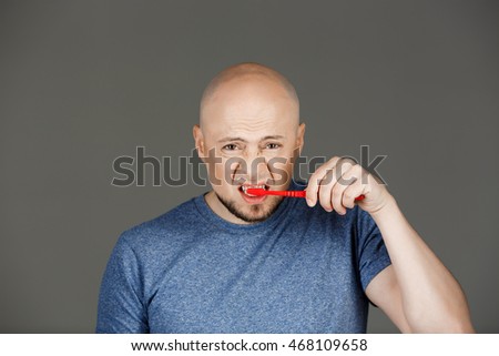 Portrait of funny handsome middle-aged man in grey shirt brushing teeth over dark background.