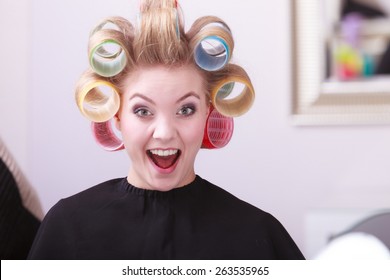 Portrait Of Funny Happy Woman In Beauty Salon. Cheerful Blond Girl With Hair Curlers Rollers By Hairdresser. Hairstyle.