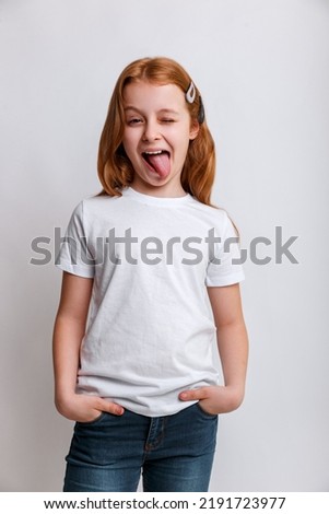 Portrait of funny kid girl smiling and showing tongue in camera wearing in white t-shirt.