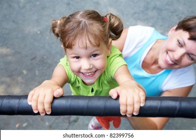 Portrait of a funny little girl hangs by horizontal bar with mother - Powered by Shutterstock