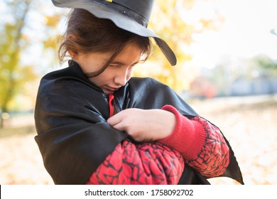 Portrait Of A Funny Little Girl Making A Sinister Face With A Paper Black Witch Hat While Walking In The Autumn Park. Halloween Meeting Concept