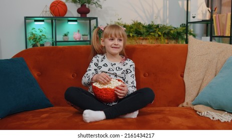 Portrait Of Funny Little Teen Children Girl Watching Entertaining Comedy Video Show Film On Tv, Eating Popcorn On Comfortable Sofa At Home Alone. Small Cute School Toddler Child Kid. Relaxation Time