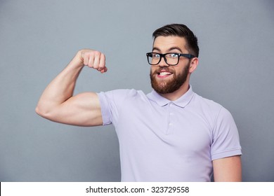 Portrait of a funny man in glasses showing his muscles over gray background