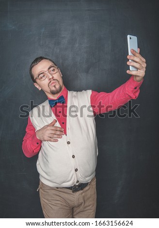 Portrait of funny nerd man making selfie on blackboard background