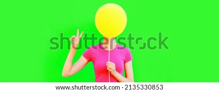 Portrait of funny woman covering her head with yellow balloon on green background