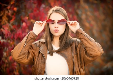 Portrait of funny woman holding autumn fall leafs. Autumn female face. Beautiful girl woman holding in her hands yellow maple leaves covering her eye.