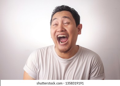 Portrait Of Funny Young Asian Man Laughing Hard With Big Open Mouth, Over White Background 