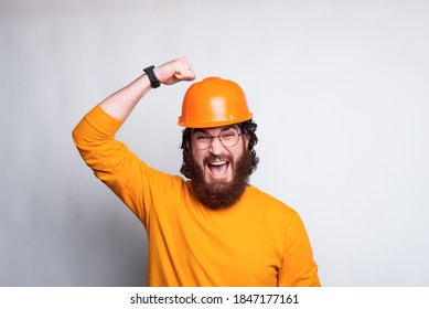 Portrait Of Funny Young Bearded Architect Hitting On Helmet, Safety First