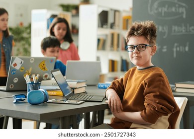 Portrait of funny young boy wearing glasses looking at camera in school library during computer class for children copy space - Powered by Shutterstock