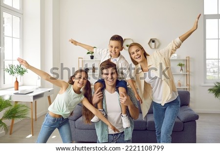 Portrait of funny young Caucasian family with children having fun and fooling around at home. Mother, daughter and father holding his son on his shoulders with outstretched arms are smiling at camera.