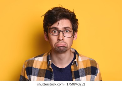 Portrait Funny Young Man In Glasses And Casual Clothes Looking At Camera Isolated Over Yellow Studio Background. Sad Nerd Guy Looks Upset, Offended, Disappointed. Bad News, Problems, Emotions Concept