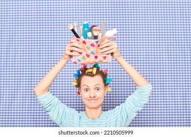 Portrait Of Funny Young Woman With Colorful Hair Curlers On Head, Holding Makeup Bag With Beauty Treatment Accessories And Cosmetics, Making Goofy Face, Fooling Arounds Over Shower Curtain Background