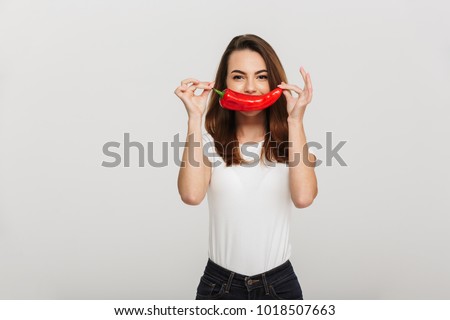 Portrait of a funny young woman holding chili pepper at her face isolated over white background