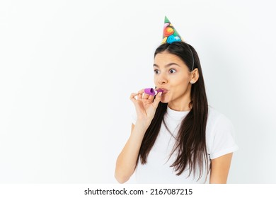 Portrait Of Funny Young Woman Wearing Birthday Cap Blowing Kazoo Pipe Standing On White Background With Copy Of Space