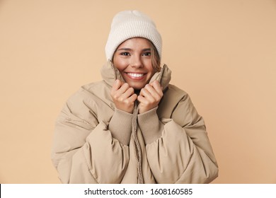 Portrait Of Funny Young Woman In Winter Coat Looking At Camera And Smiling Isolated Over Beige Background