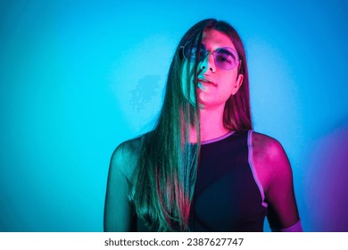 Portrait of a futuristic transgender person with long hair and sunglasses illuminated by neon lights - Powered by Shutterstock