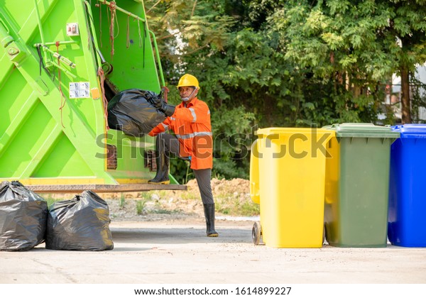 Portrait of garbage collector with truck loading\
waste and trash bin.
