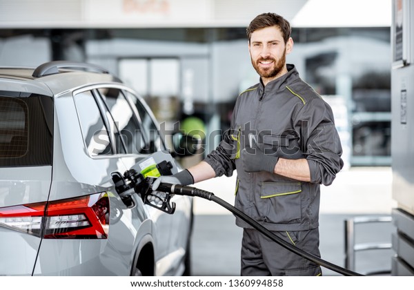 Portrait of a gas station worker\
in workwear refueling luxury car with gasoline at the\
station