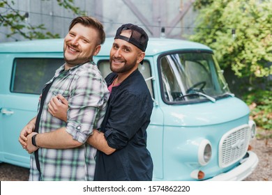 Portrait Of A Gay Couple In Front Of An Old-fashioned Car Van. Boyfriends Hug And Smile To The Camera.