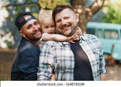 Portrait Of Gay Family In The Yard. Happy Fathers And Their Little Daughter Giving Smiles To The Camera.