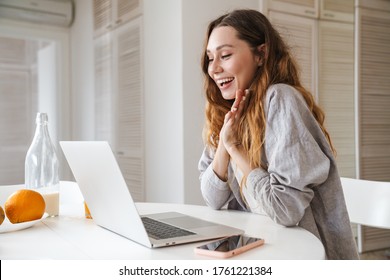 Portrait Of Ginger Excited Woman Expressing Surprise While Working With Laptop In Bright Kitchen