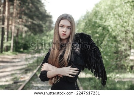 Portrait of girl black angel image in wings posing in mysterious forest, looking at camera. Young lady at fairy tale woodland. Vintage retro image, fantasy concept. Copy space for advertising text