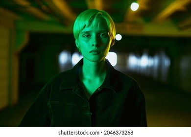 Portrait Of A Girl In A Black Shirt And With A Short Haircut Who Stands In An Empty Parking Lot In A Neon Green Light. High Quality Photo