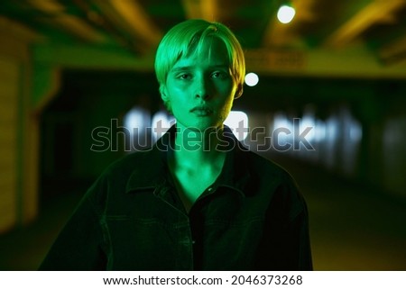 portrait of a girl in a black shirt and with a short haircut who stands in an empty parking lot in a neon green light. High quality photo