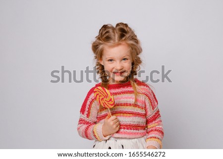 portrait of a girl a blonde child with a Lollipop on a stick smiling in colored clothes on a white background