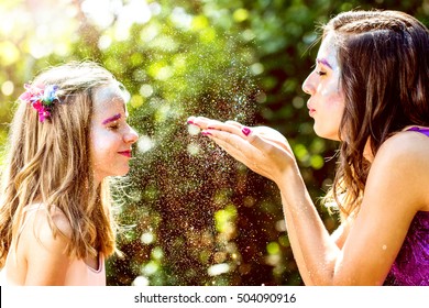 Portrait Of Girl Blowing Gold Glitter Towards Younger Kid In Forest.