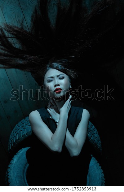 Portrait of a\
girl in blue contrasting lighting, posing in a Studio sitting with\
car tires. Futuristic neon\
lighting