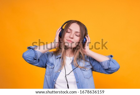 Portrait of a girl in casual clothes, who is happy to listen to music on headphones on a yellow background. Student listening to music with headphones with eyes closed, isolated on yellow background.