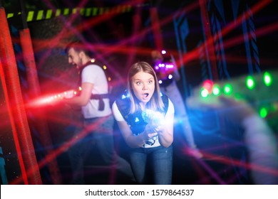 Portrait of girl in colored beams of laser guns during laser tag game on dark arena