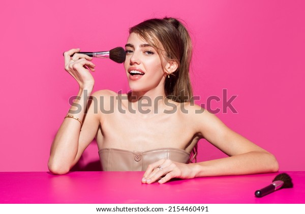 Portrait of a girl with cosmetic brush near face.\
Woman holds makeup brush. Portrait of beautiful female model\
holding makeup blusher brush, clean face, isolated background.\
Cosmetics and makeup.