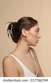 Portrait of a girl with dark hair. The lady's hair is fixed with a white hair clip decorated with pearls. The woman in a white shirt and earrings is posing on the beige bac - Shutterstock ID 2177362749