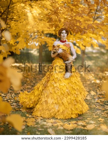 Portrait of a girl in a dress made of autumn maple leaves with a red fox in her arms