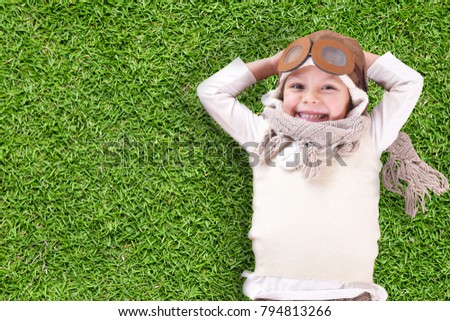 Portrait of a girl, dressed as a pilot or aviator with a hat and glasses, lying in the grass and she dreams with open eyes and thinks about the future. Concept of: success, future, dreams