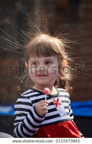 Portrait of a girl with electrified hair on a dark background. Little girl holding a chupa chups with a stick. Electricity power concept.