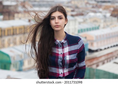 portrait of girl with fluttering long black hair in a checkered shirt on a rooftop