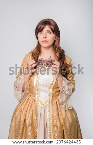 Portrait of a girl in a golden rococo gown with a crown in his hands posing isolated on a white background.