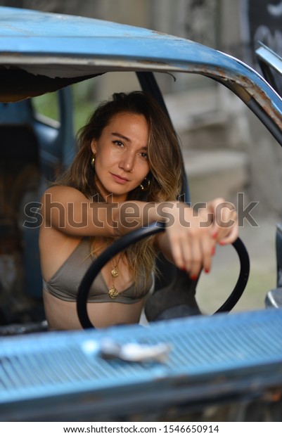 portrait of girl in green bra,
camouflage print pants and necklace near the blue old car in the
street